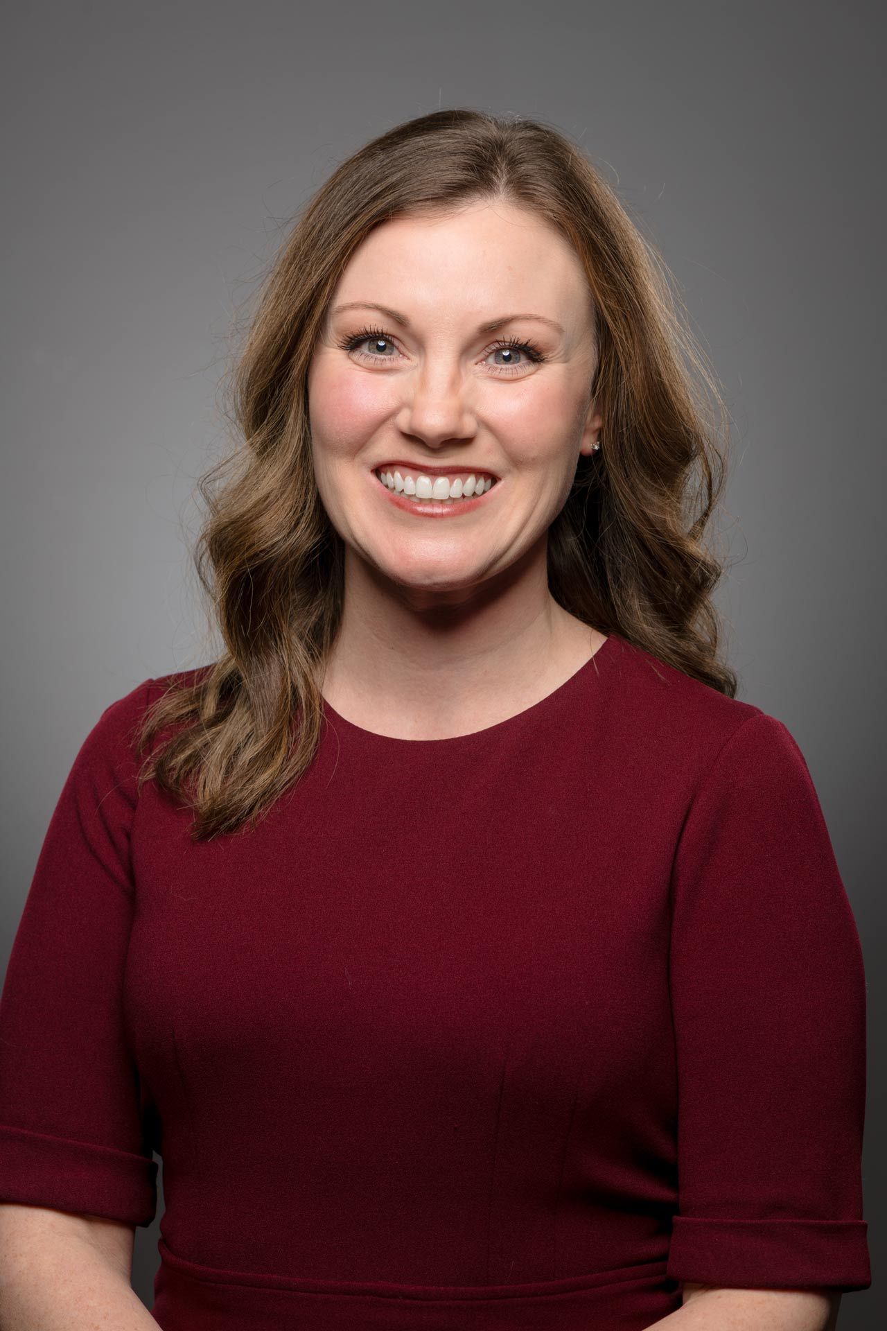 A woman in a blue shirt is standing with her arms crossed and smiling.