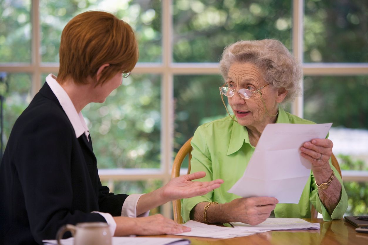A woman is sitting at a table talking to an older woman who is holding a piece of paper.