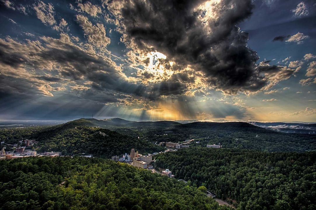 Aerial view of forested mountains with a town in the valley below under a partly cloudy sky.