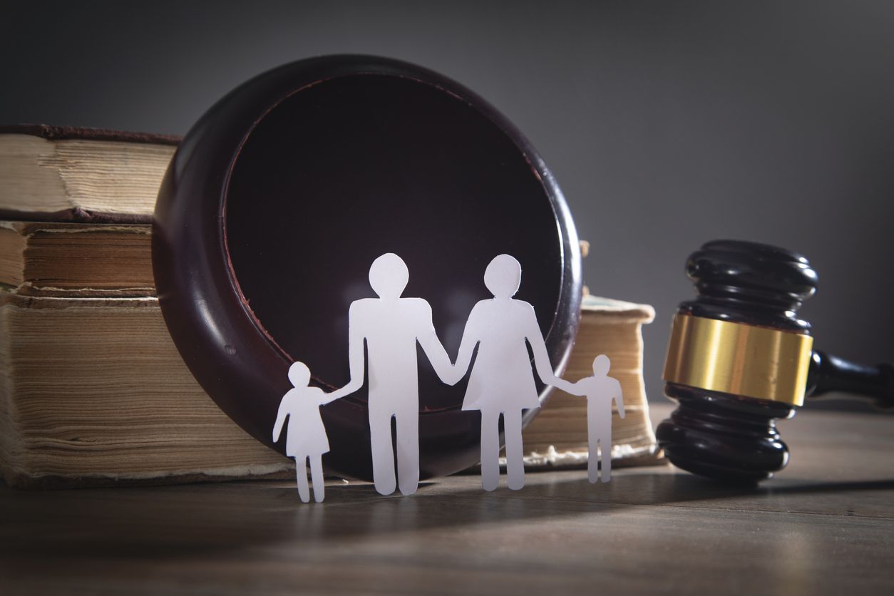 A paper cut out of a family holding hands next to a judge 's gavel and a book.
