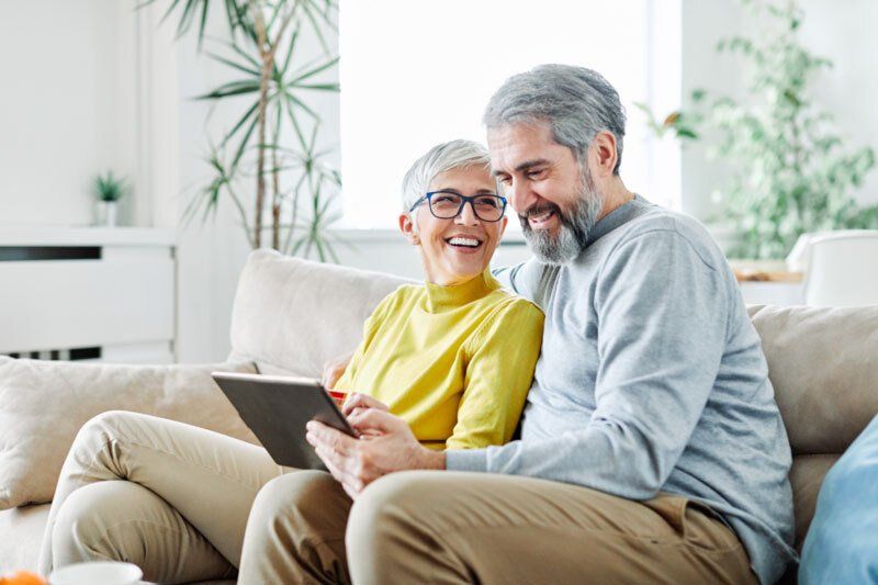 A man and a woman are sitting on a couch looking at a tablet.