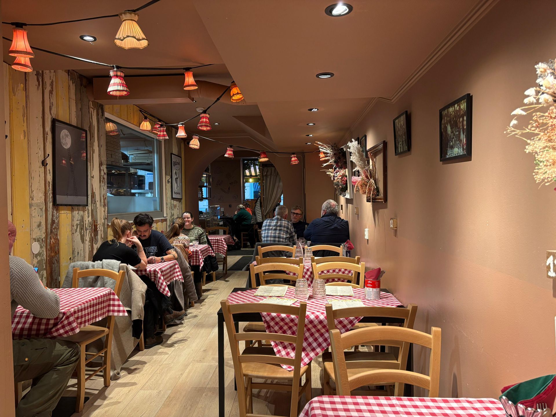 Restaurant interior with red checkered tablecloths, patrons dining, and string lights.