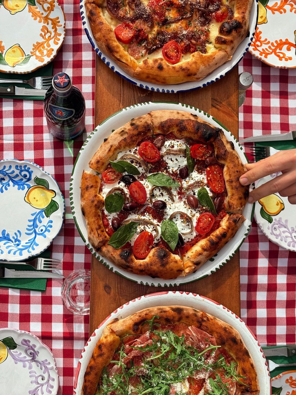 Four women in floral outfits, one on a red scooter, others eating pasta, Italian flag in background.