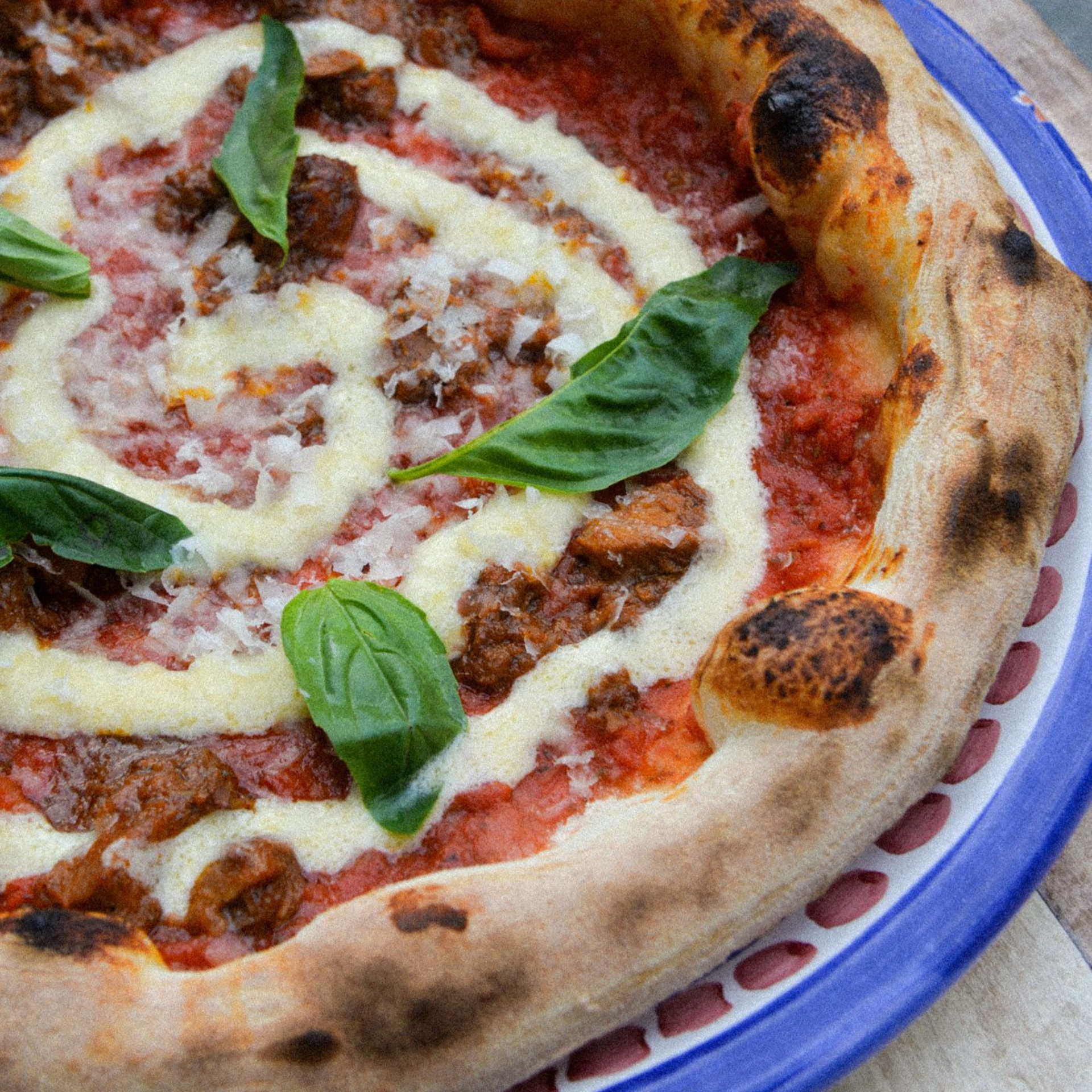 Pizza with spiral of white sauce, ground meat, basil, and charred crust, on a blue plate.