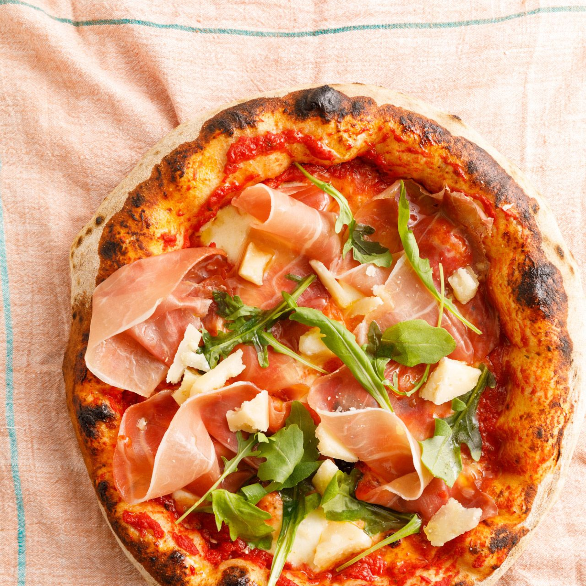 Pizza with tomatoes, olives, anchovies, and basil on a blue plate, outside on a wooden surface.
