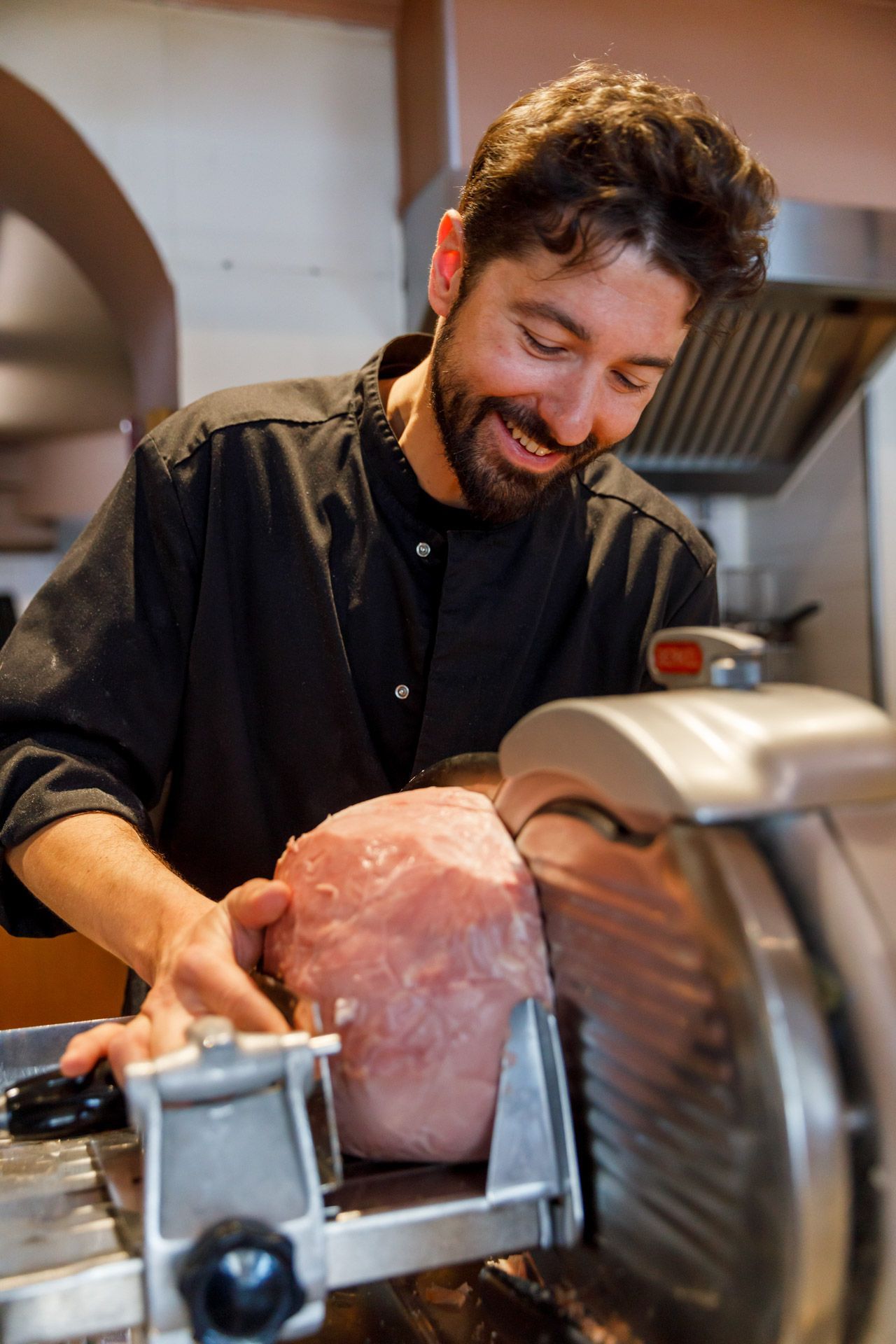 Chef smiling as he slices a large ham with a meat slicer.