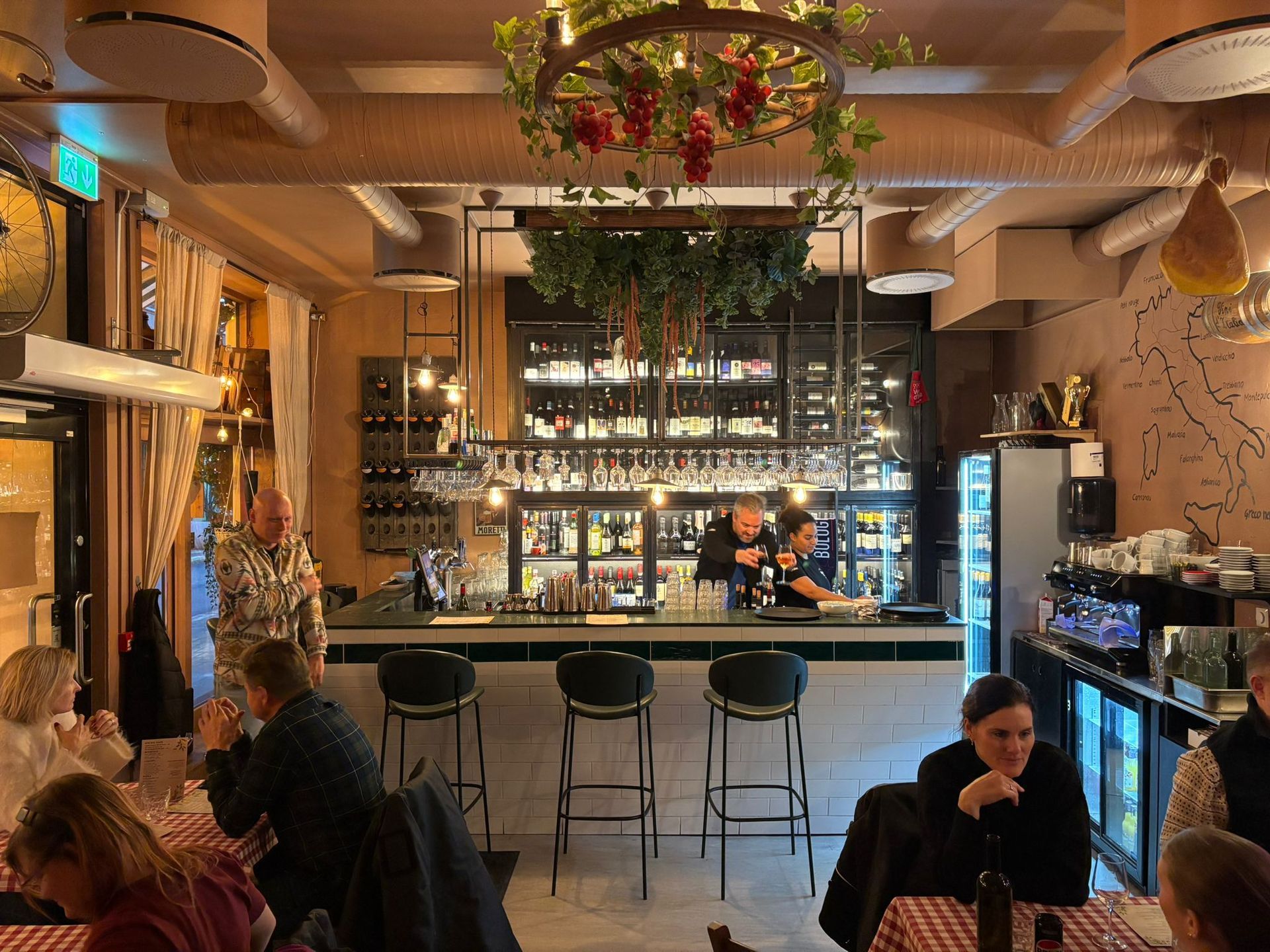Restaurant interior with bar, patrons, and staff behind the bar, olive green barstools.