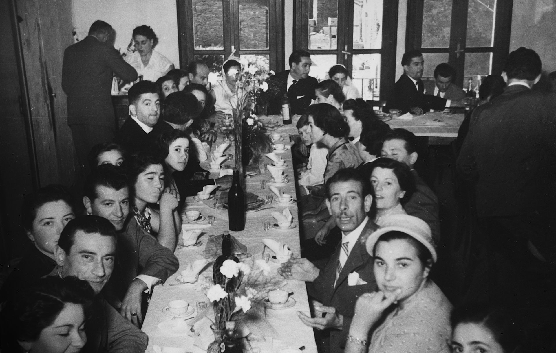 Black and white photo of a crowded banquet table with people, possibly at a gathering or celebration.
