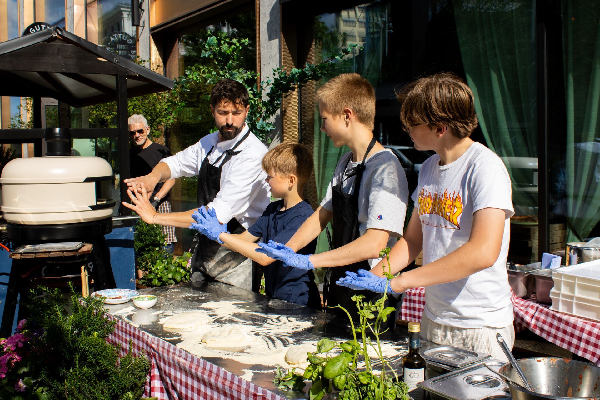 Chef and three boys making pizza outdoors.