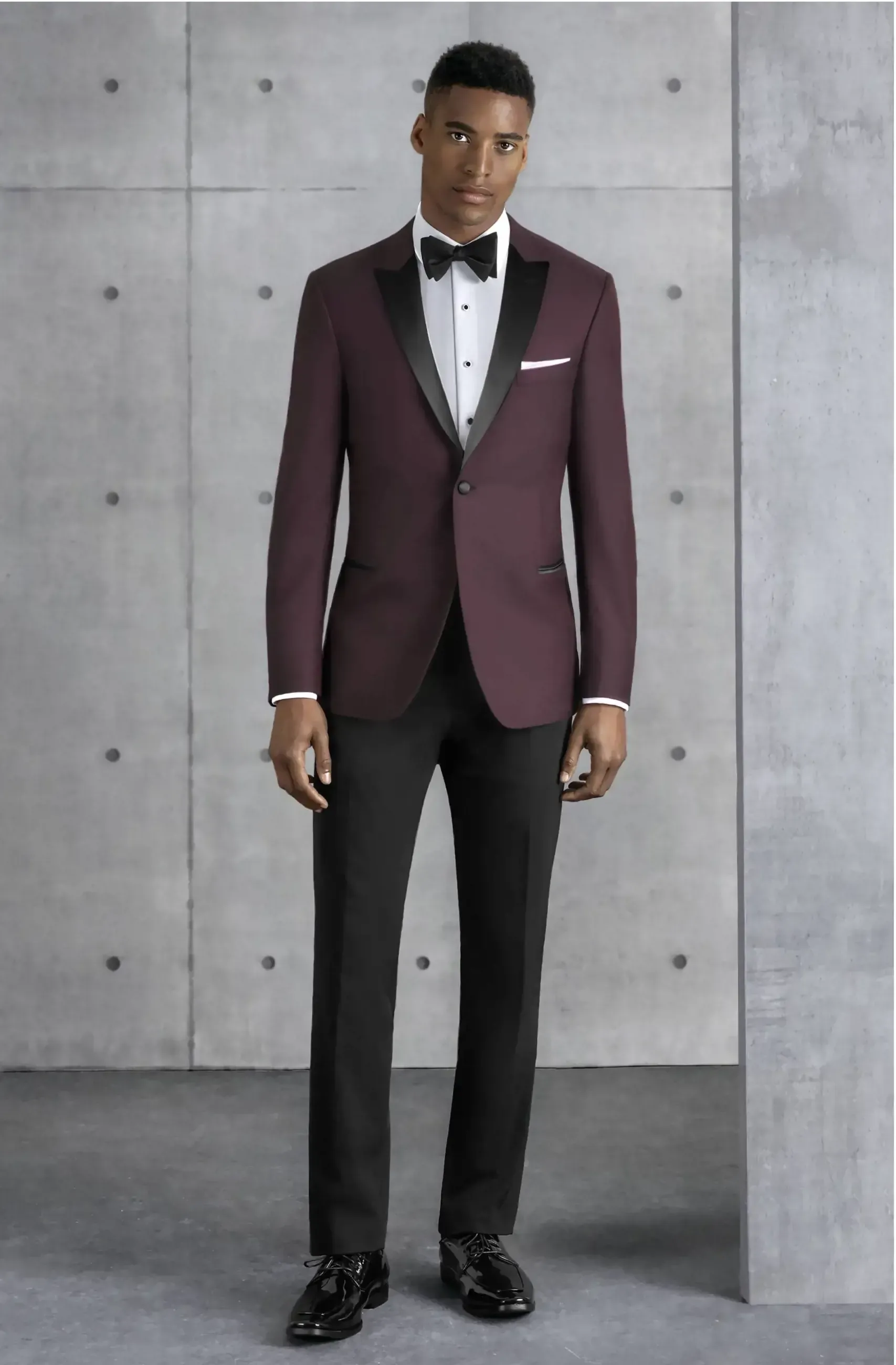 A man is wearing a burgundy tuxedo and black pants.