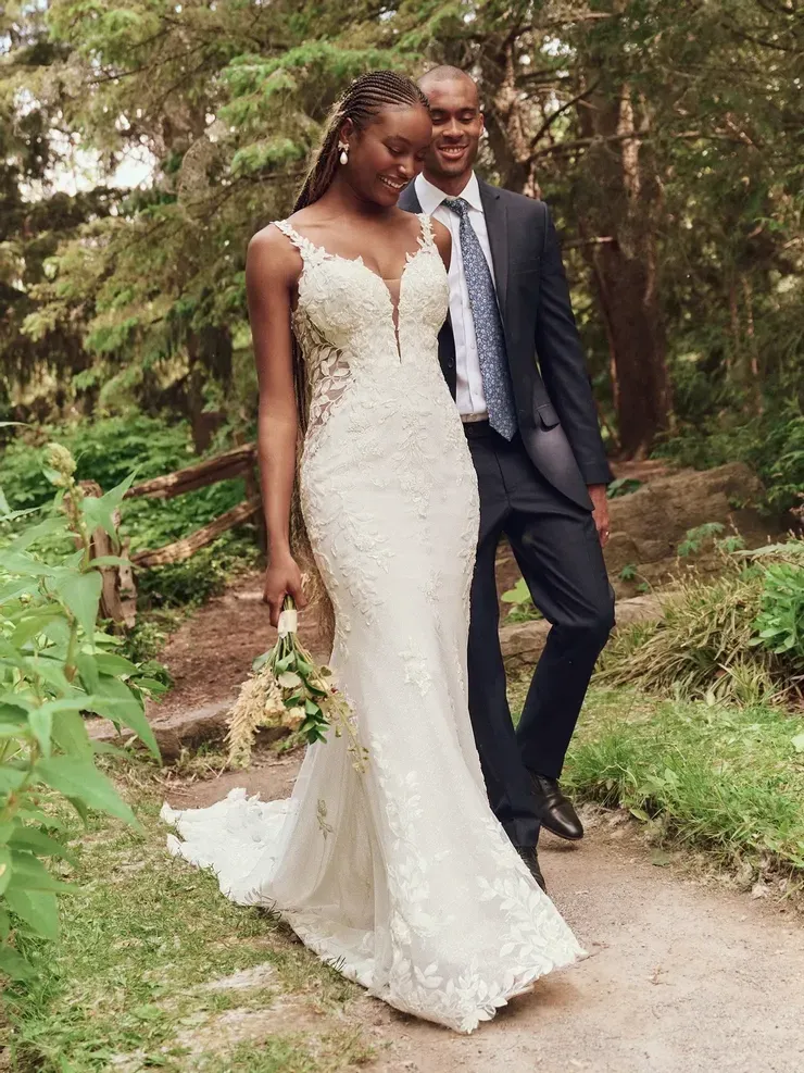 A bride and groom are walking down a path in the woods.
