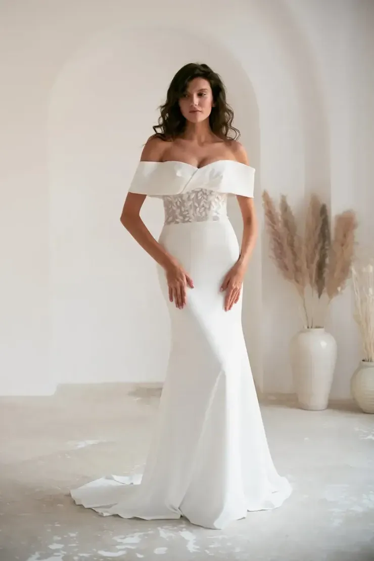 A woman is wearing a white off the shoulder wedding dress.