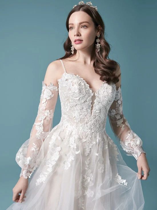 A woman is wearing a white lace wedding dress with long sleeves.