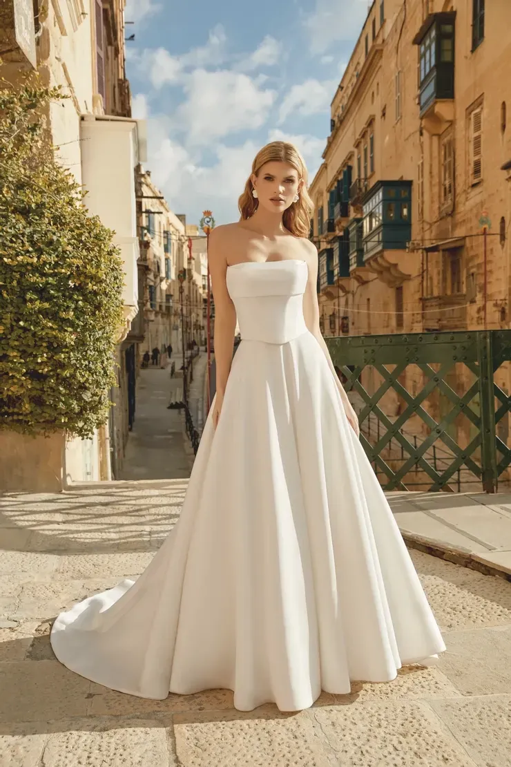 A woman in a white wedding dress is standing on a sidewalk in front of a building.