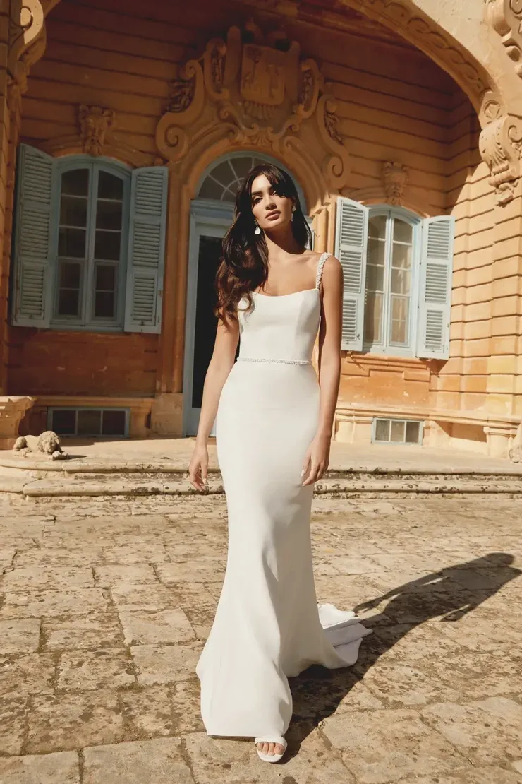 A woman in a white dress is standing in front of a building.