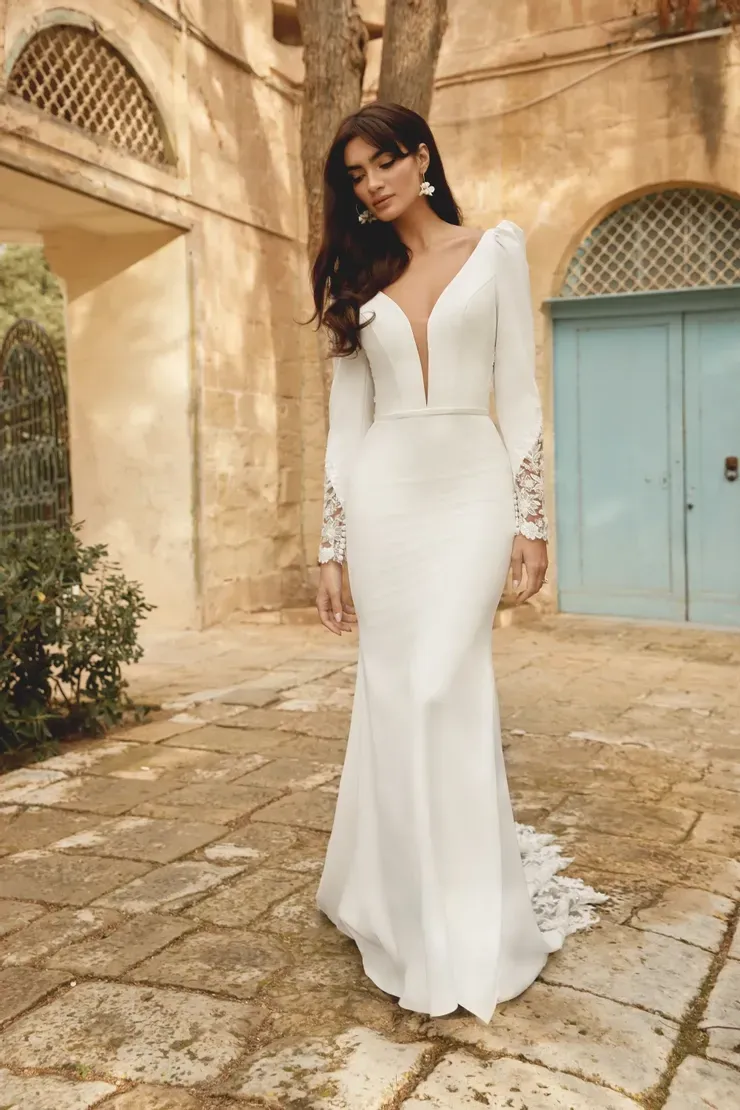 A woman in a white wedding dress is standing in front of a building.