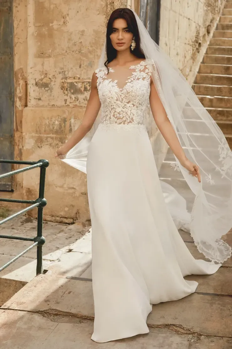 A woman in a white wedding dress and veil is standing in front of a building.