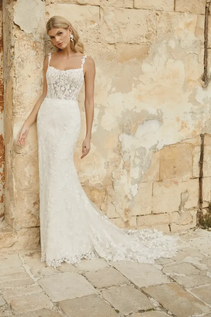 A woman in a white wedding dress is standing in front of a brick wall.