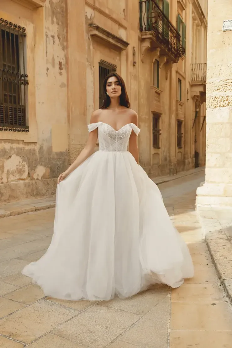 A woman in a white wedding dress is standing on a sidewalk in front of a building.