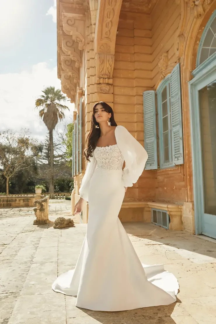 A woman in a white wedding dress is standing in front of a wooden building.