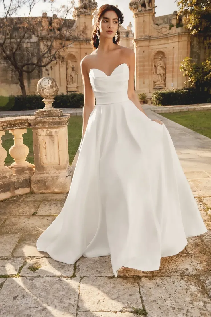 A woman in a white wedding dress is standing in front of a building.