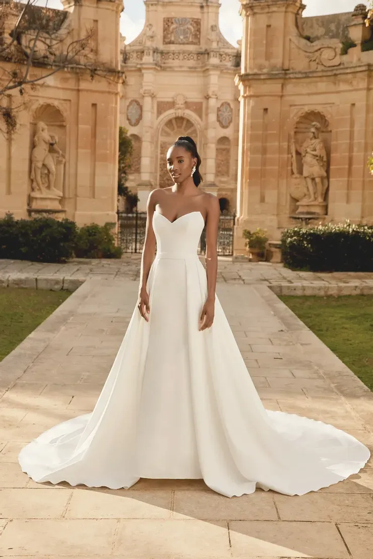 A woman in a white wedding dress is standing in front of a building.