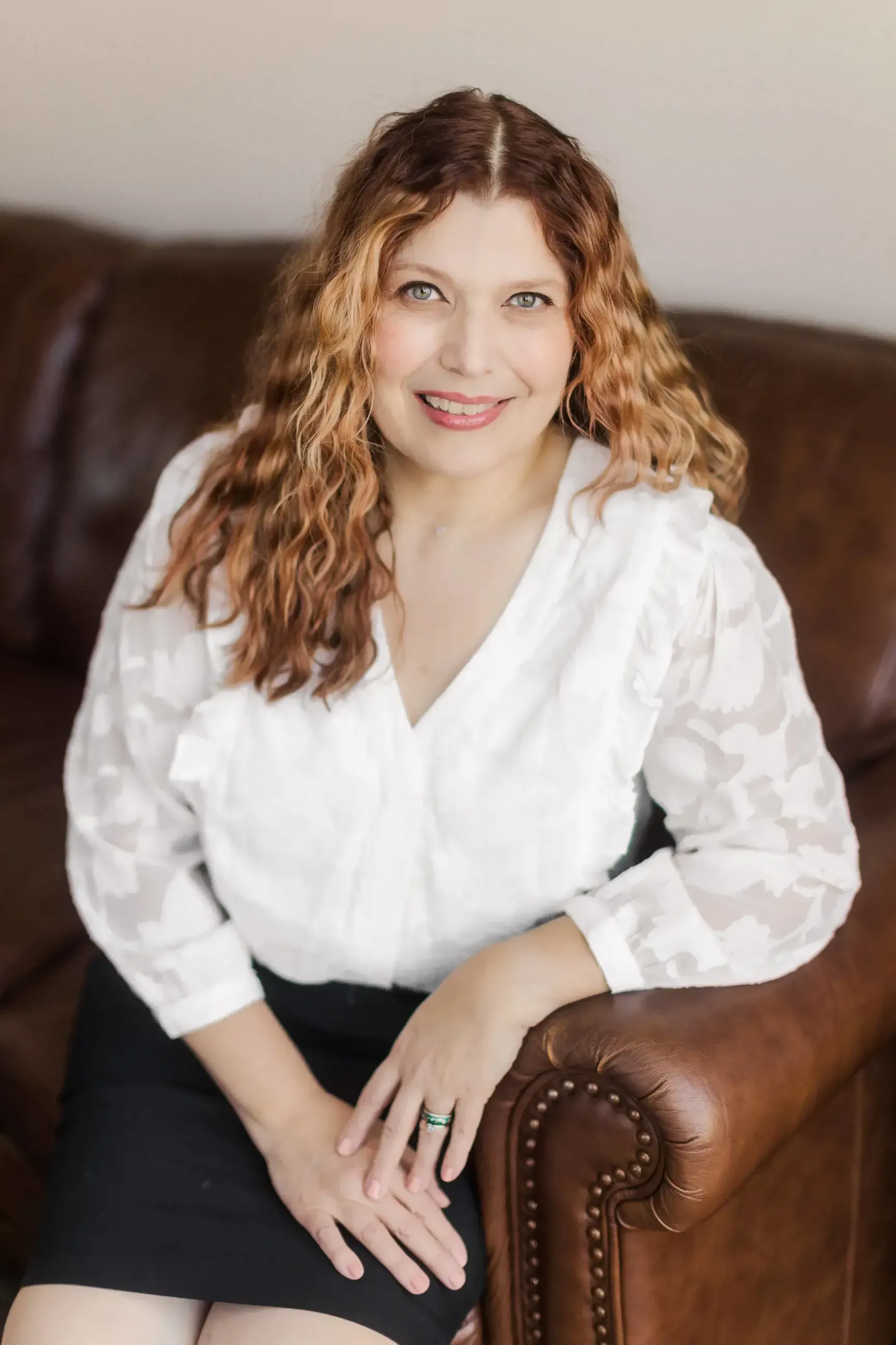 A woman in a white shirt is sitting on a brown couch.