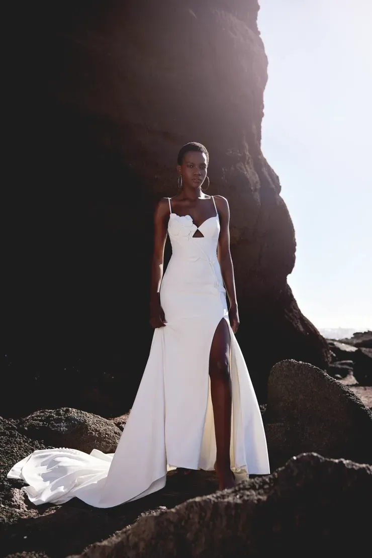 A woman in a white dress is standing on a rocky beach.