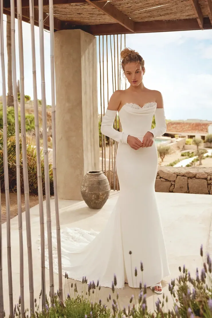 A woman in a white wedding dress is standing in front of a fence.