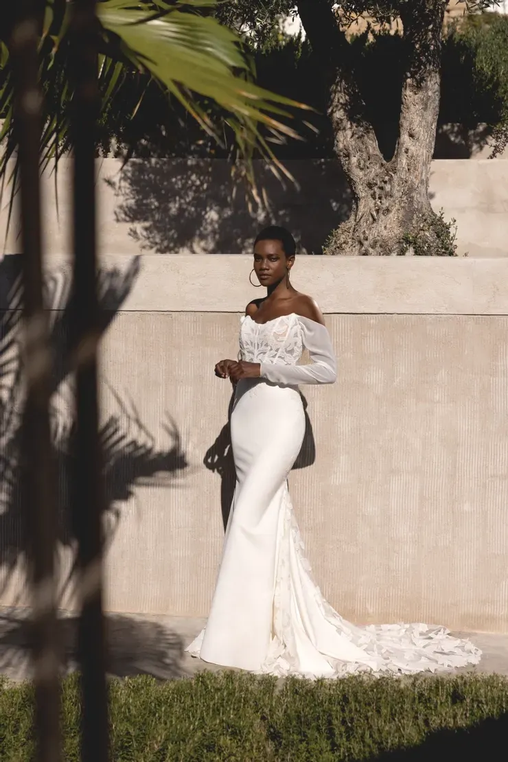 A woman in a white dress is standing in front of a wall.