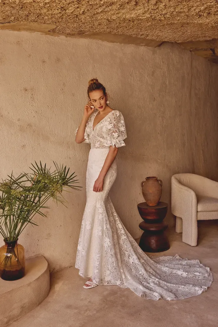 A woman in a wedding dress is standing in a room next to a chair.