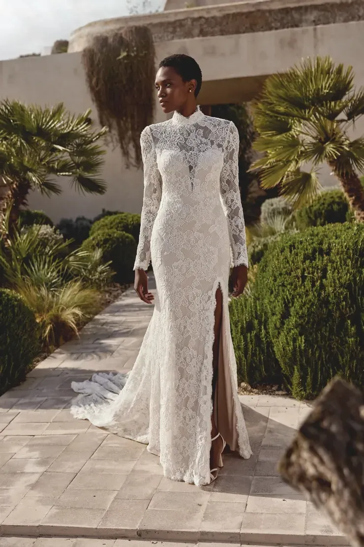 A woman is wearing a white lace wedding dress with long sleeves and a high slit.