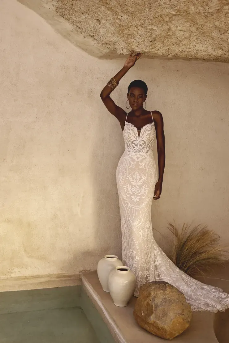 A woman in a wedding dress is standing next to a rock.