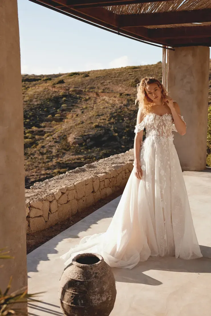 A woman in a white wedding dress is standing next to a vase.