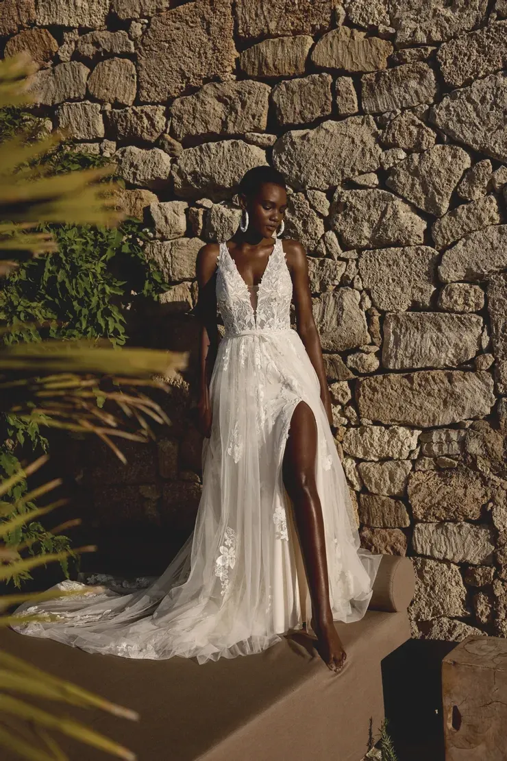 A woman in a wedding dress is sitting on a bench in front of a stone wall.