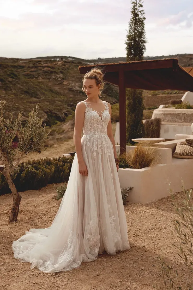 A woman in a wedding dress is standing in the dirt in front of a building.