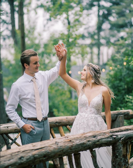 A bride and groom are standing on a wooden bridge holding hands.