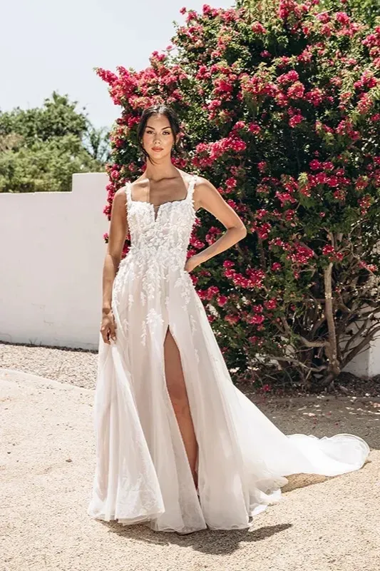 A woman in a wedding dress is standing in front of a bush with pink flowers.