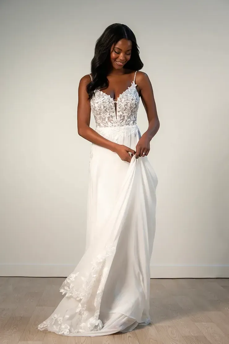 A woman in a white wedding dress is standing in front of a white wall.