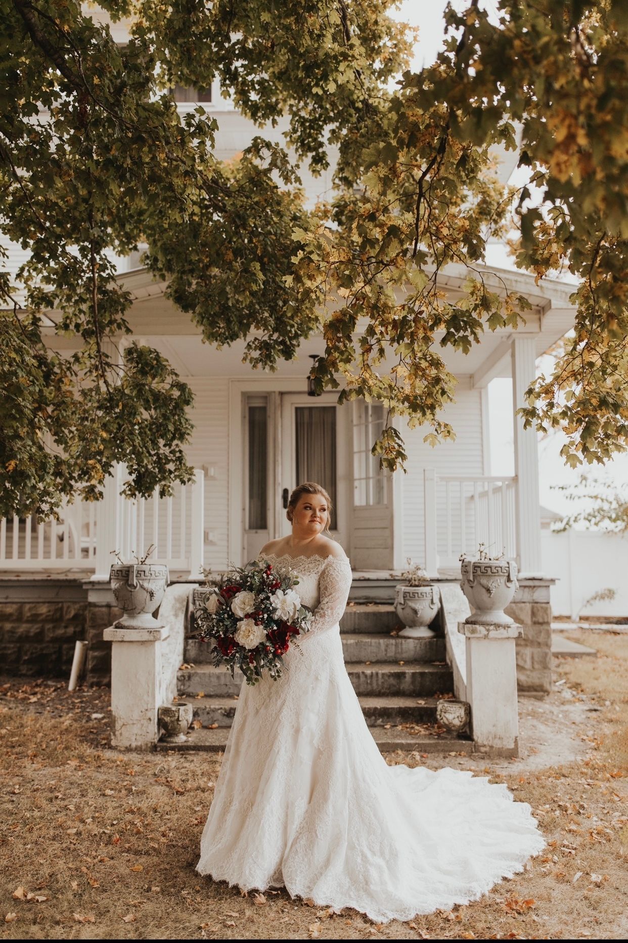 A bride in a wedding dress is standing in front of a white house holding a bouquet of flowers.