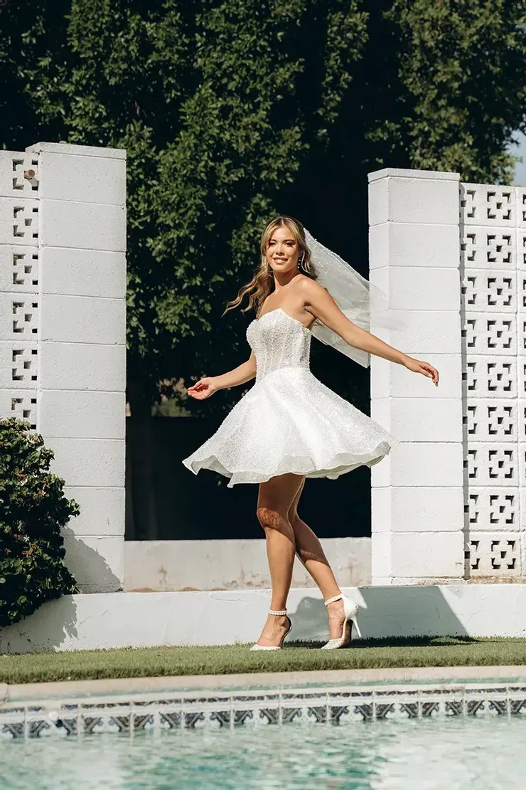 A woman in a white dress and veil is standing next to a pool.