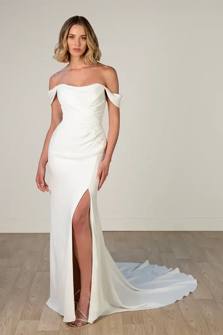 A woman is wearing a white off the shoulder wedding dress with a high slit.