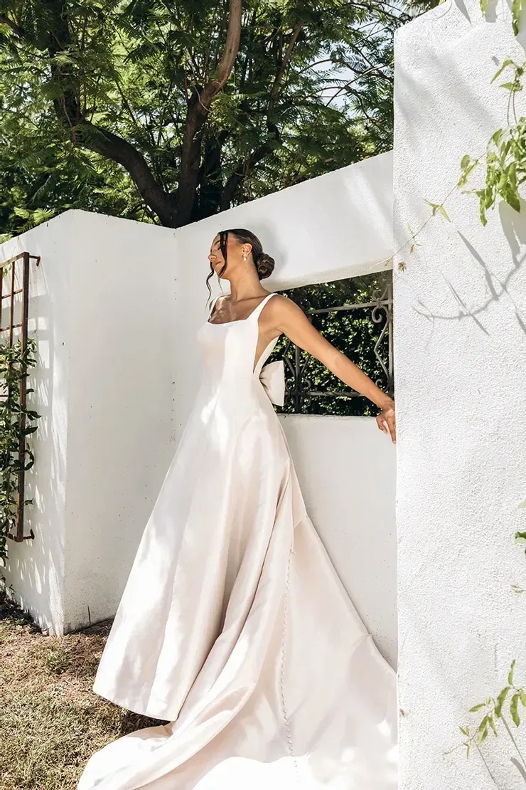 A woman in a wedding dress is standing in front of a white wall.