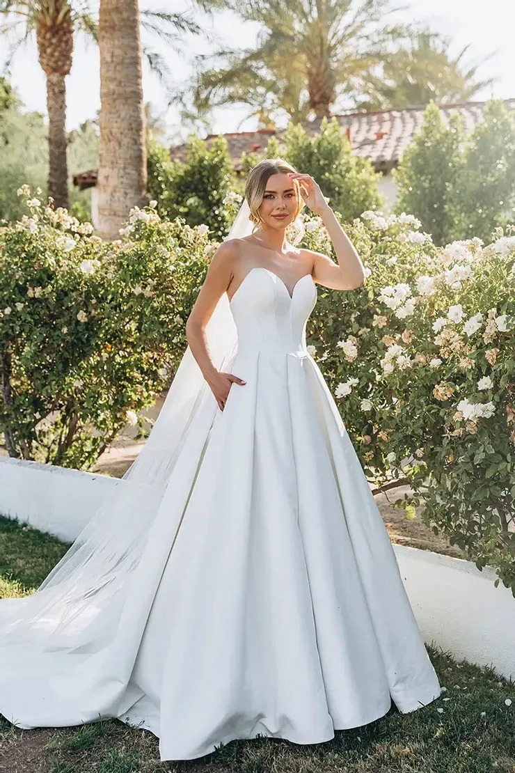 A woman in a white wedding dress is standing in front of a bush.