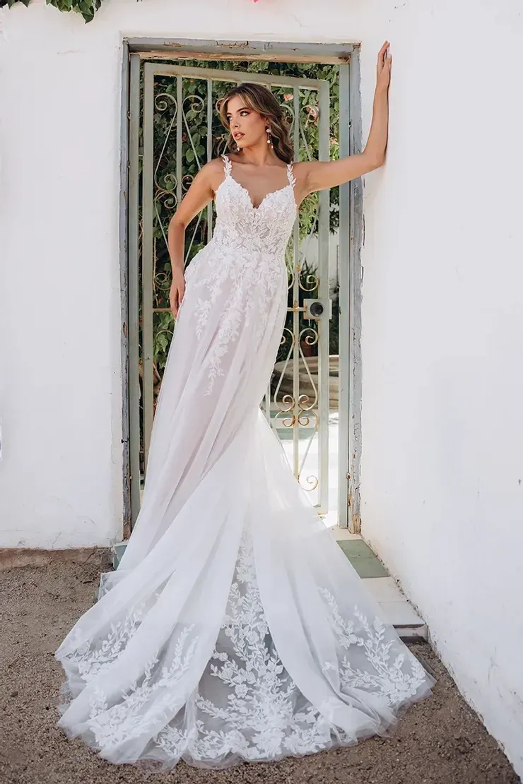 A woman in a white wedding dress is standing in front of a white building.