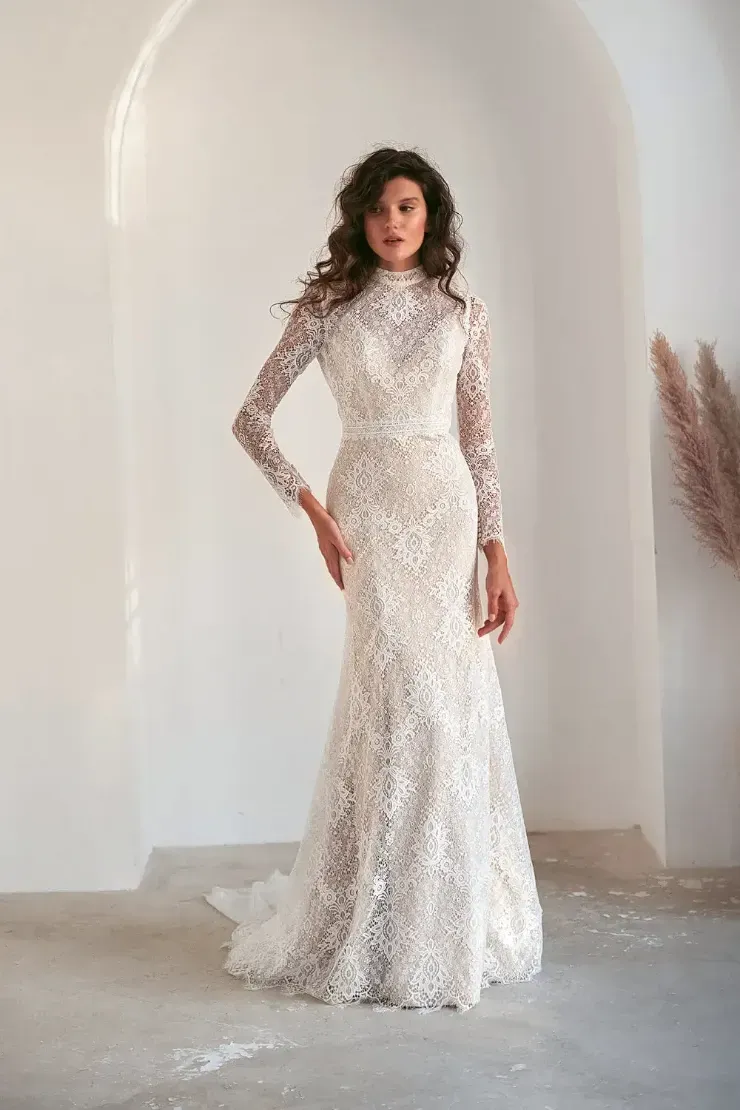 A woman is wearing a white lace wedding dress with long sleeves.