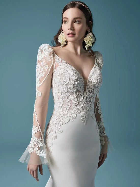 A woman is wearing a white wedding dress with long sleeves and earrings.