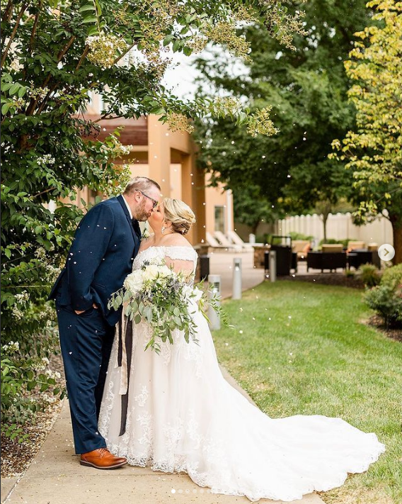 A bride and groom are kissing on a sidewalk.
