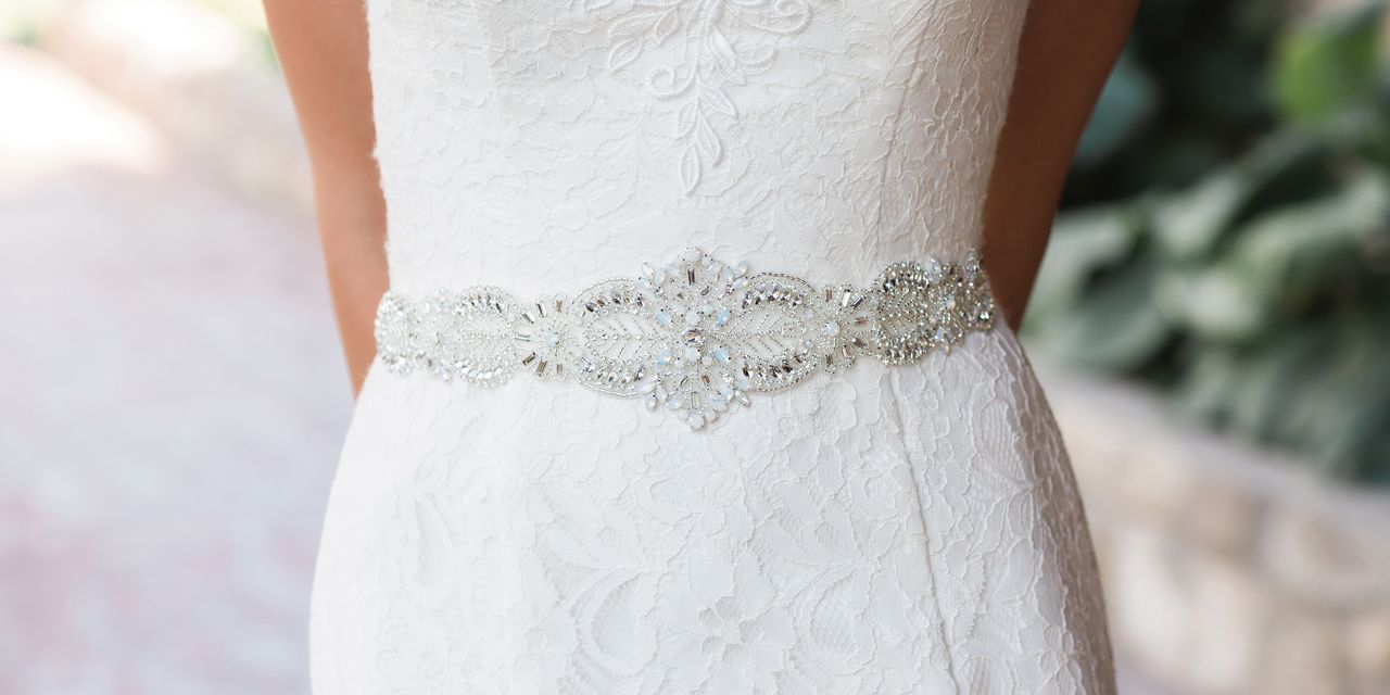 A woman is wearing a white wedding dress with a rhinestone belt.