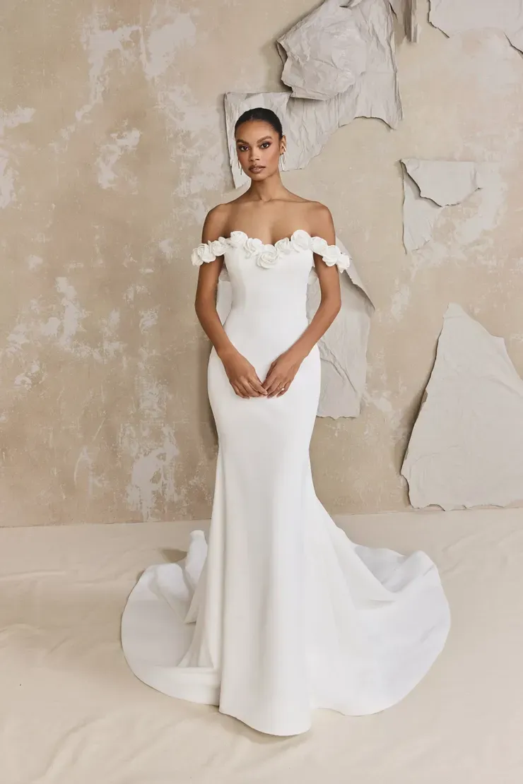 A woman in a white wedding dress is standing in front of a wall.